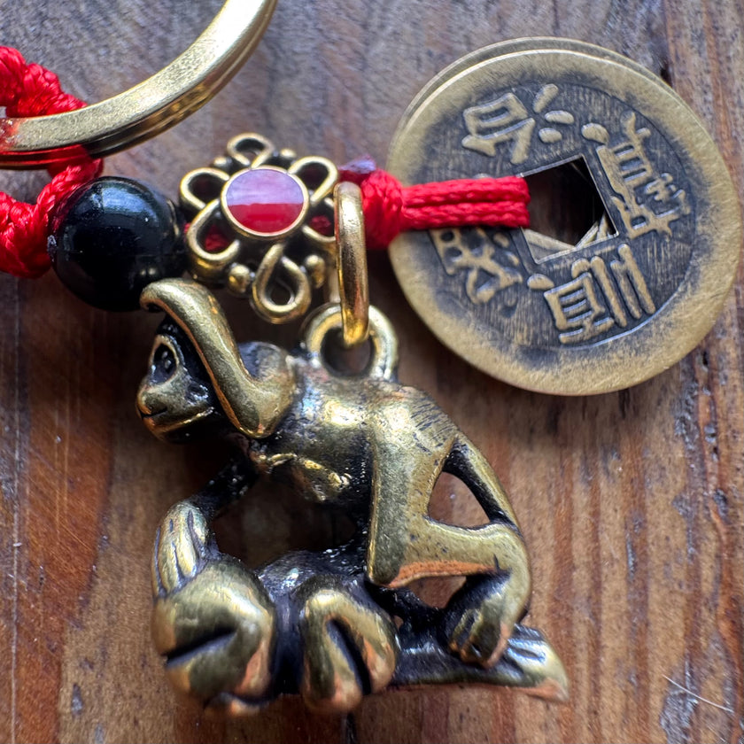 Brass monkey charm on a red string with a Chinese coin on a wooden surface