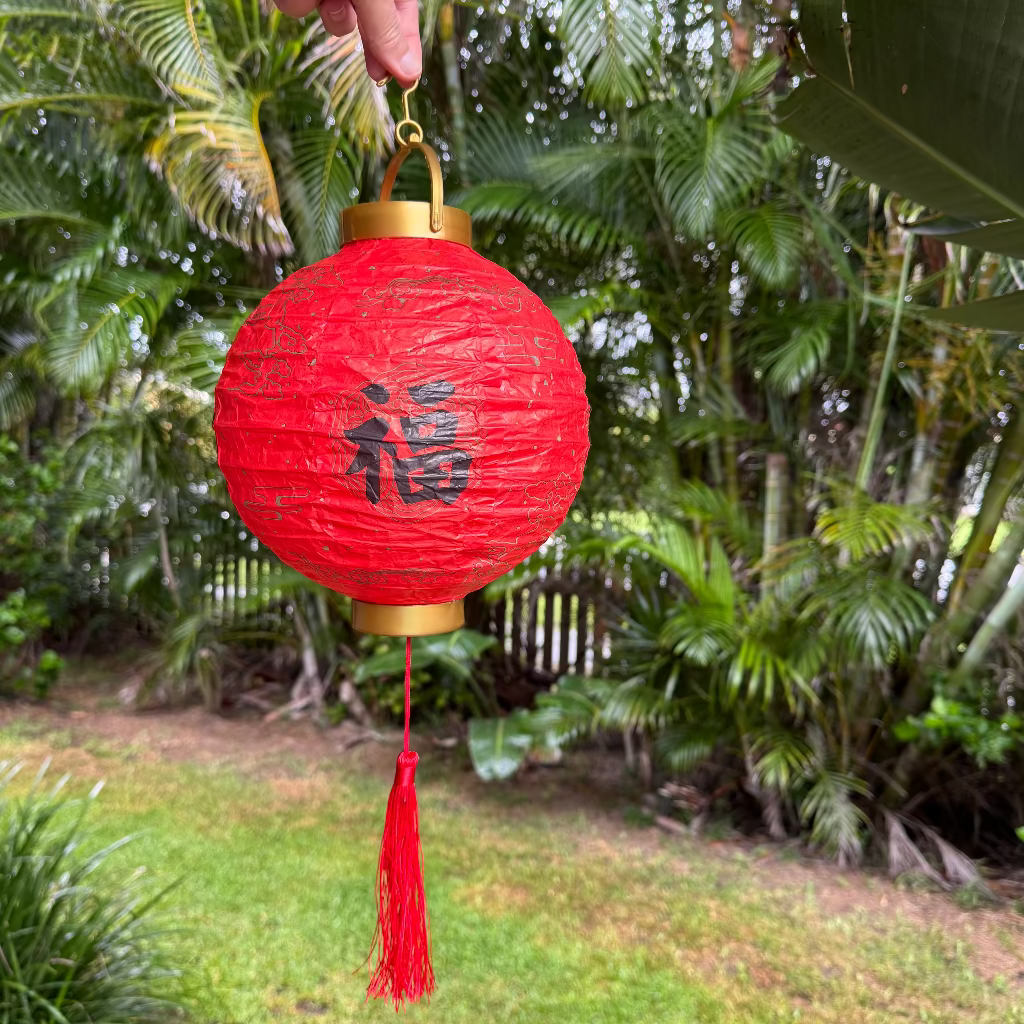 A red Chinese LED paper lantern with a tassel tail and Chinese characters on it, hanging outdoors.