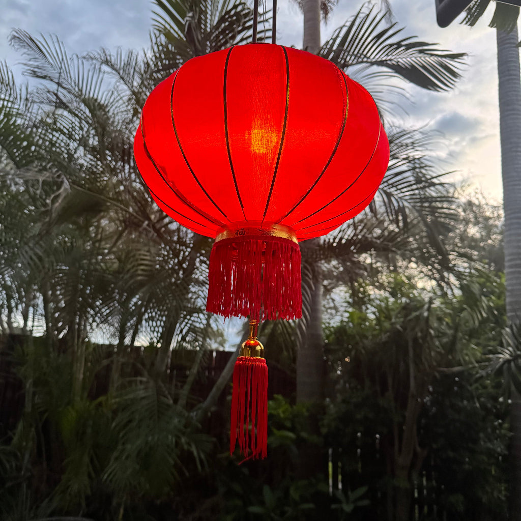 red satin Chinese lantern with gold decoration hanging in garden
